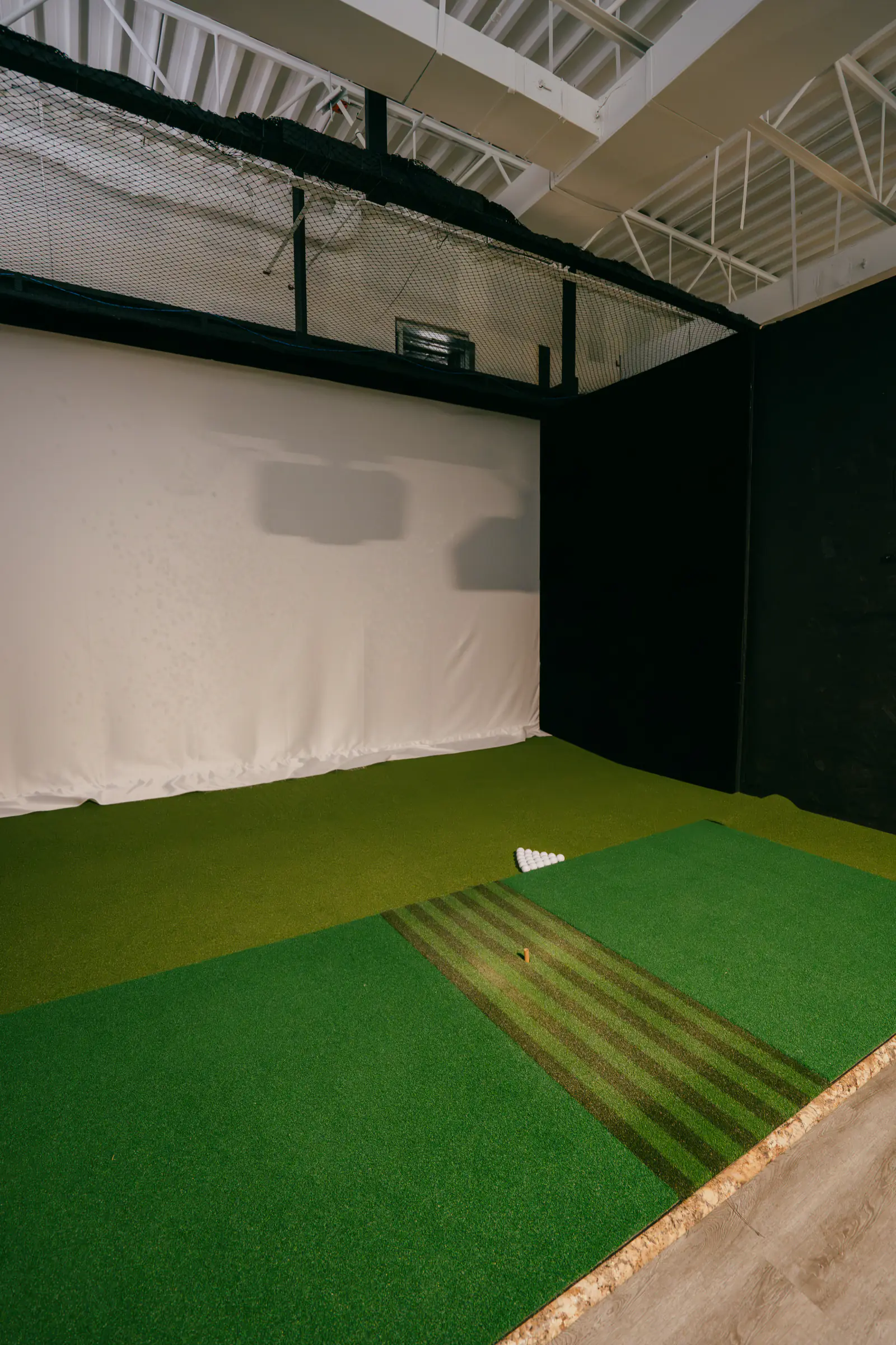 An empty PGM simulator bay with the hitting mat, tee strip and projection screen
