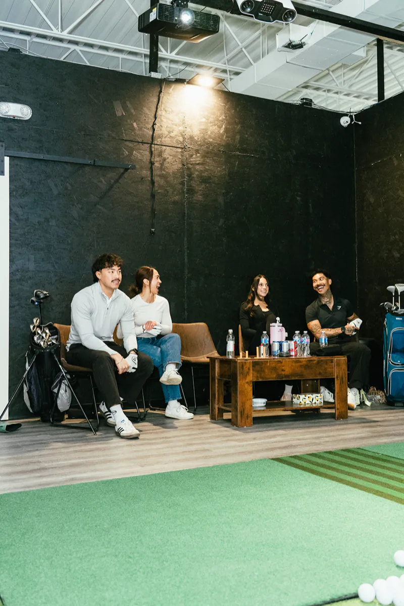 Four friends sit and chat on the chairs beside the hitting mat in a bay