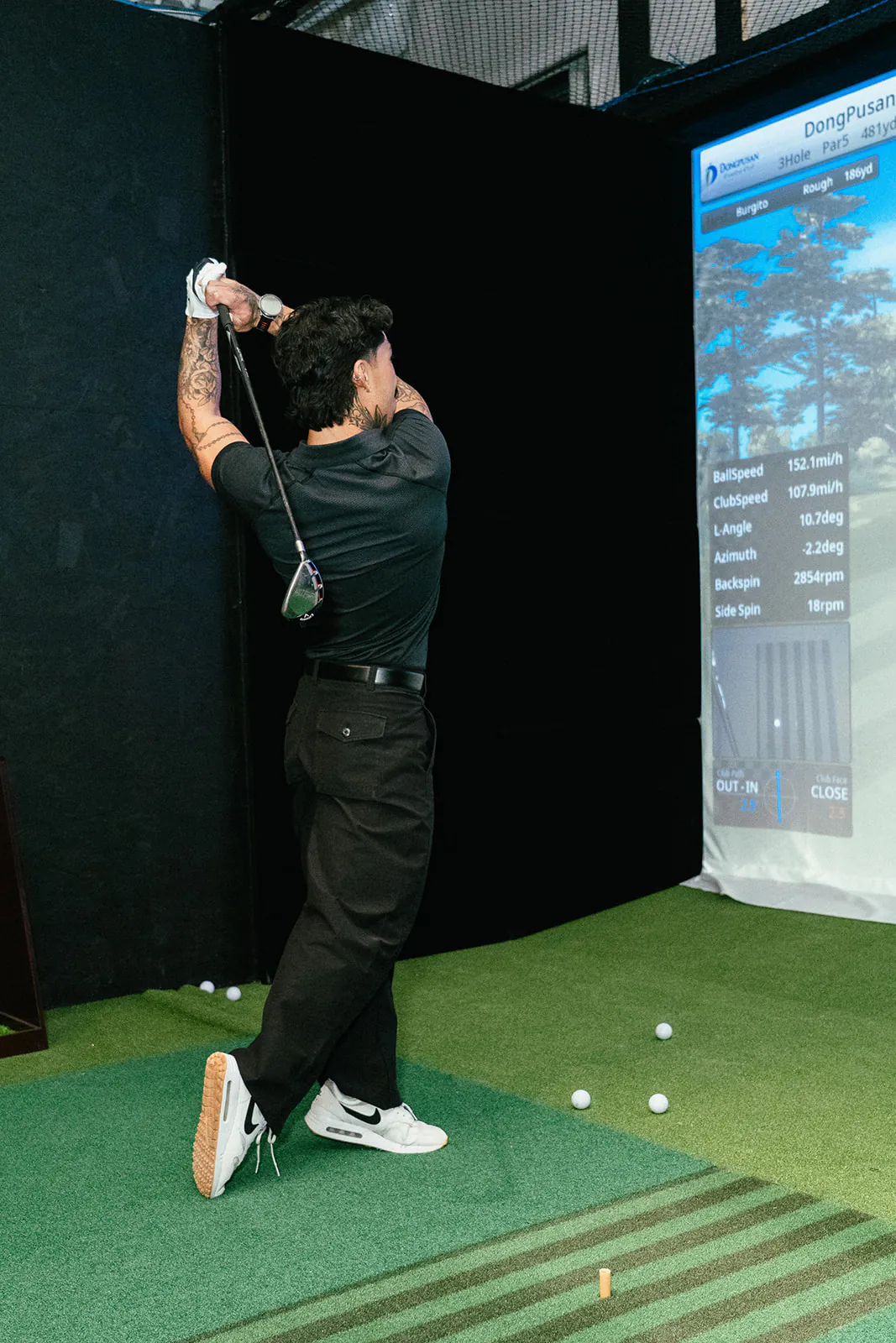 A golfer swings on the hitting mat in a PGM simulator bay with the course on screen
