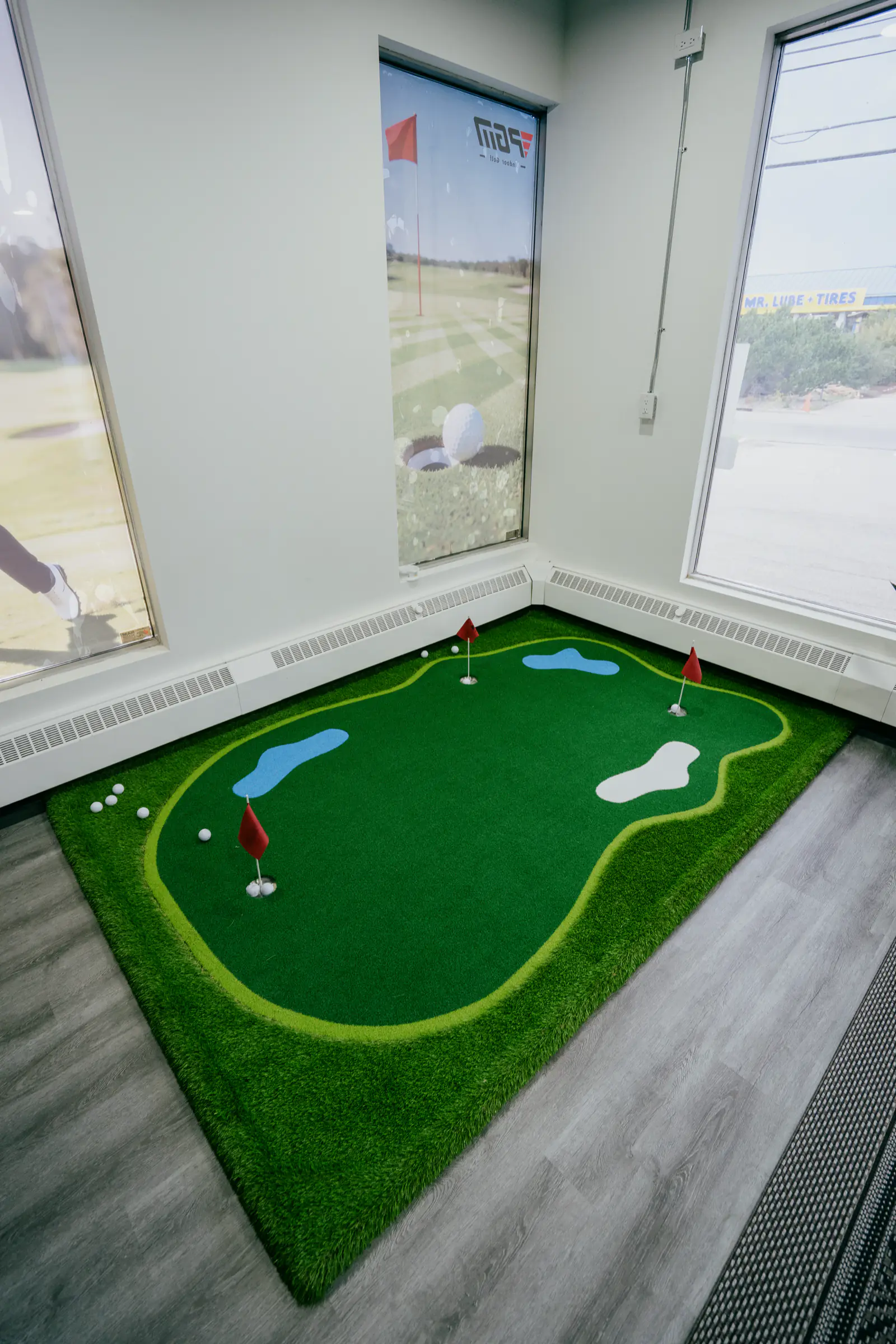 The indoor putting green at PGM Indoor Golf Calgary, with flags and daylight through the windows