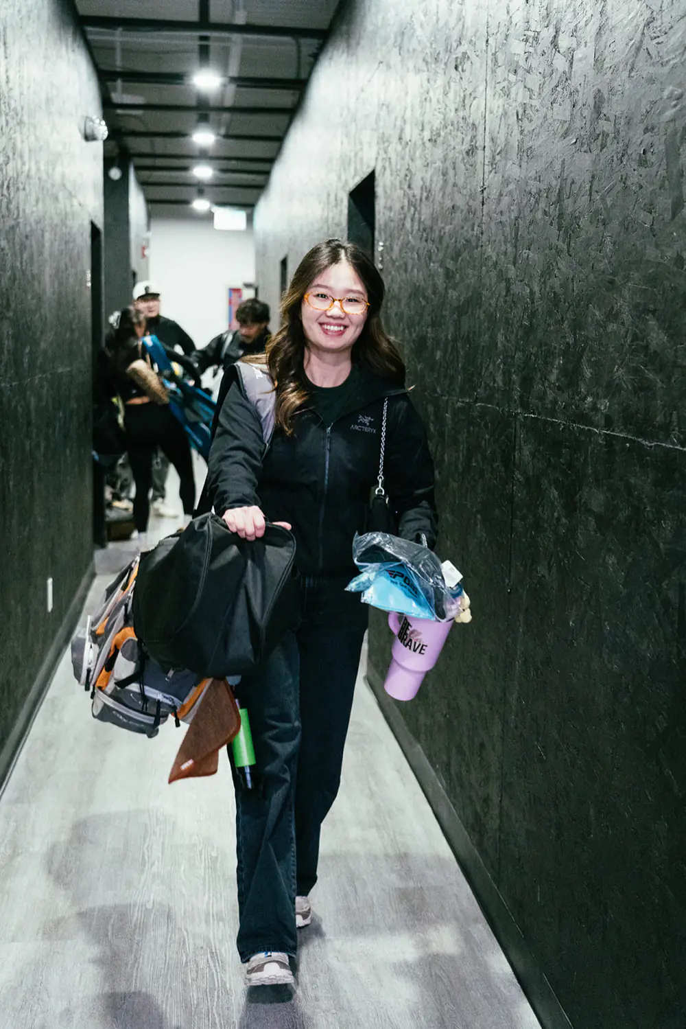 A golfer carries her clubs down the hallway to a PGM bay with others behind her